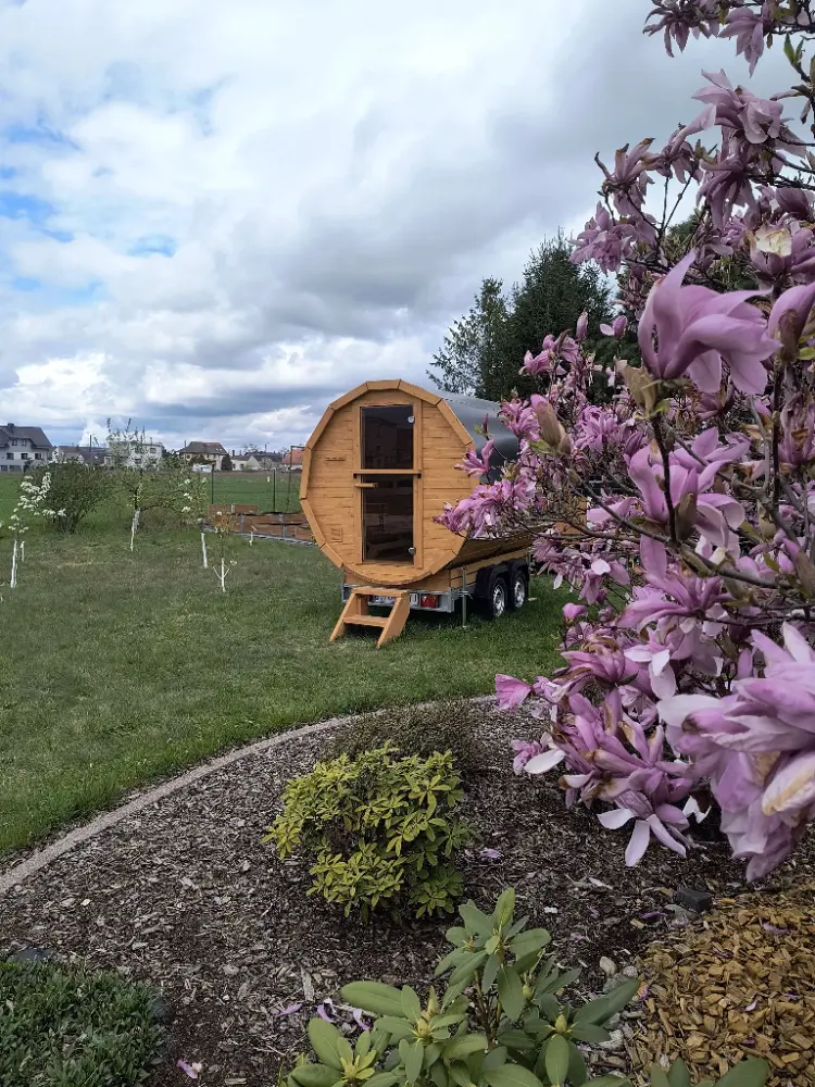 Mobilna sauna w ogrodzie wśród kwitnących krzewów